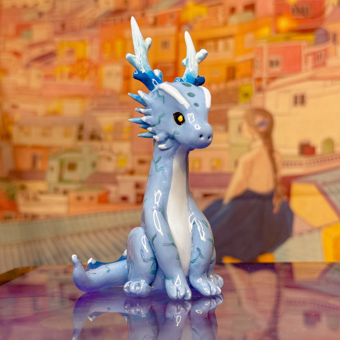 Blue korean dragon figurine on a reflective surface with a colorful cityscape in the background