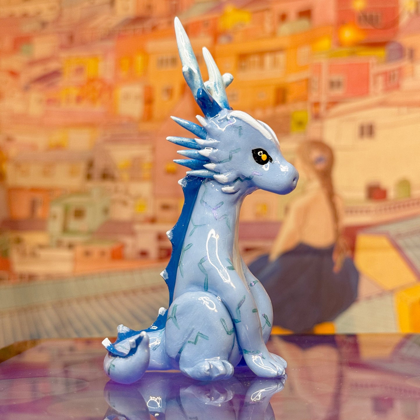 Blue dragon figurine on a reflective surface with a colorful, blurred background