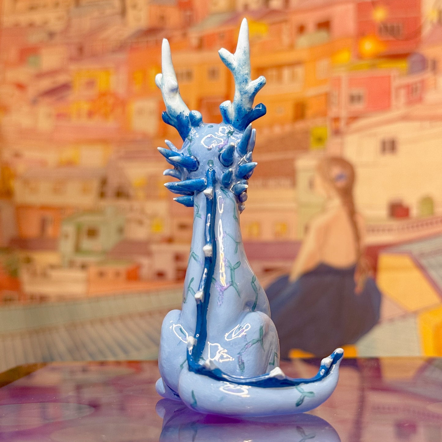 Decorative blue and white dragon figurine on a reflective surface with a colorful abstract background.